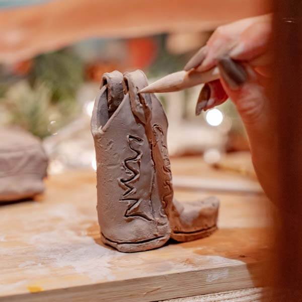 A cozy clay crafting session with a small figure in progress being shaped with a wooden tool, using Sculpd Pottery Kit